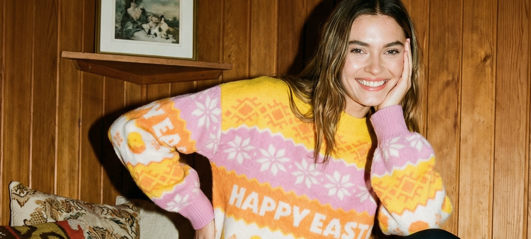 Smiling woman in a pink and yellow Happy Easter knit sweater against wood paneling