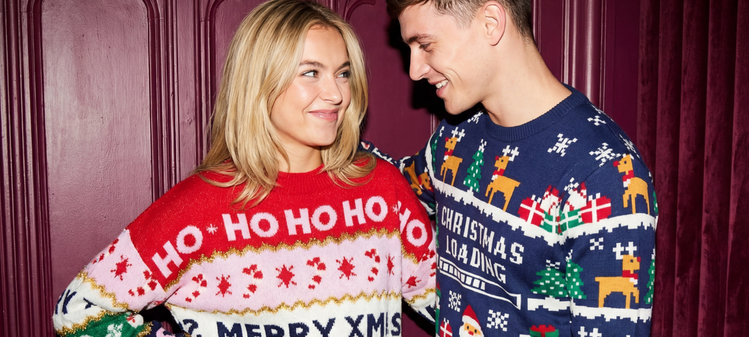 Smiling couple wearing festive Christmas jumpers and looking at each other against a deep red backdrop